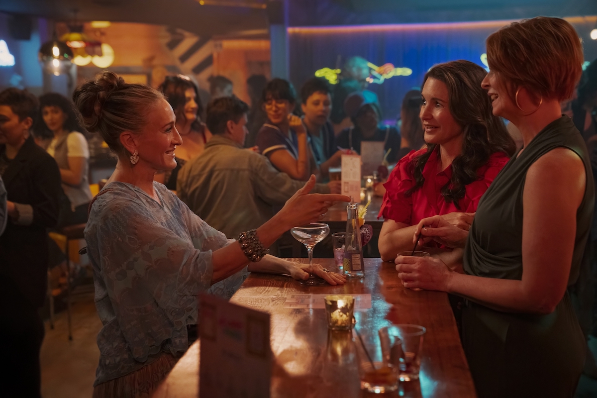 Sarah Jessica Parker, Kristin Davis, and Cynthia Nixon in 'And Just Like That' Season 3, shown here standing at a table in a crowded bar