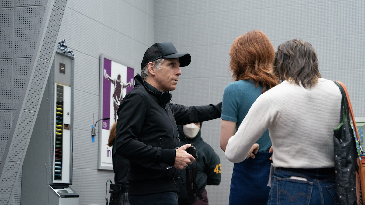 Ben Stiller on the set of 'Severance,' wearing a black baseball cap, holding a camera, talking to Britt Lower