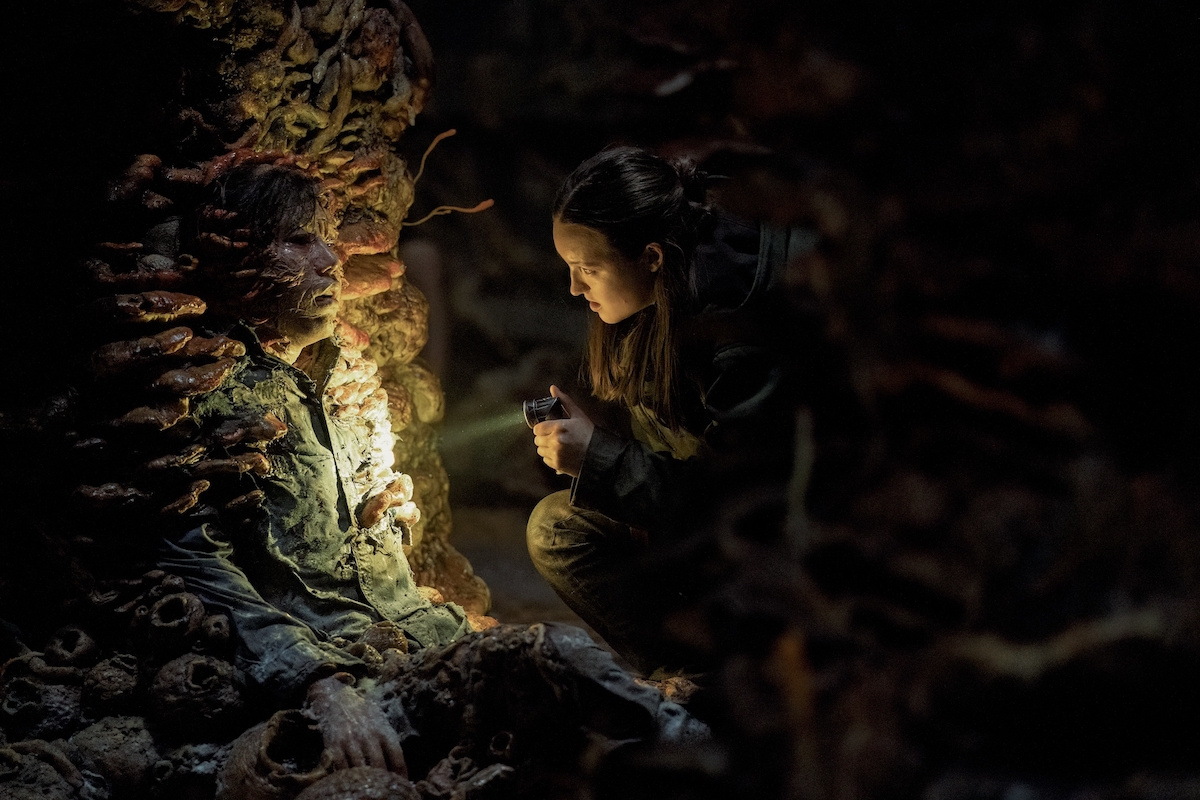Bella Ramsey in 'The Last of Us' Season 2 Episode 5, shown examining a body consumed by fungus