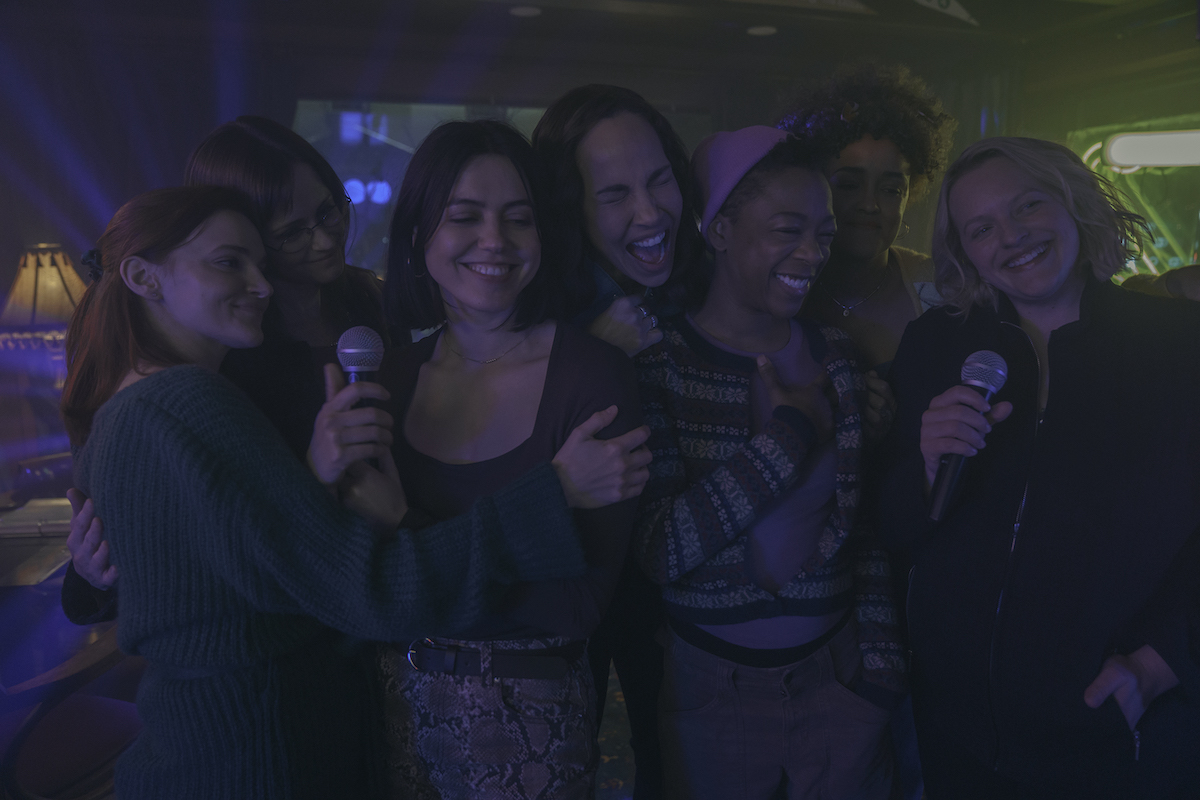 THE HANDMAID’S TALE Season 6 Episode 10 stars [L to R] MADELINE BREWER, ALEXIS BLEDEL, NINA KIRI, AMANDA BRUGEL, SAMIRA WILEY, BAHIA WATSON, ELISABETH MOSS, shown here singing karaoke in a dark bar, smiling