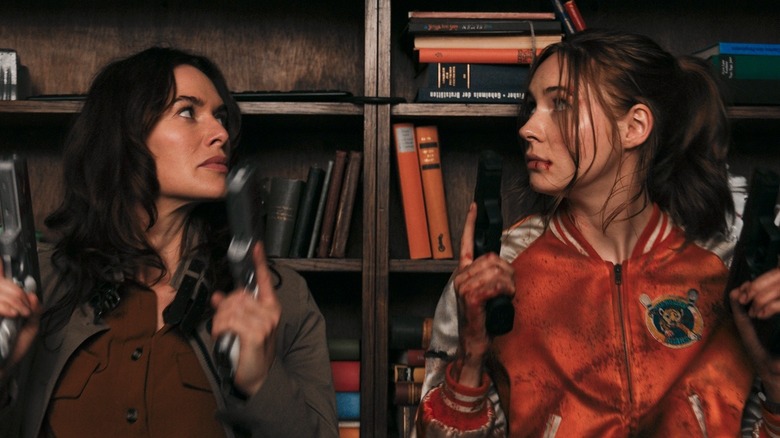 Scarlett and Sam with guns behind a shelf of books in Gunpowder Milkshake (2021)