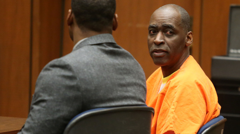 Michael Jace sits next to a lawyer in court, wearing an orange prison uniform
