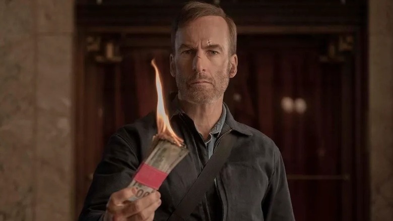 Hutch holding a burning stack of cash in Nobody (2021)