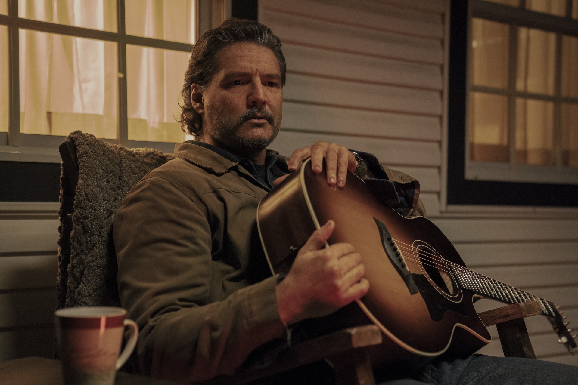 Pedro Pascal sitting in a rocking chair holding a guitar in 'The Last of Us' Season 2. 