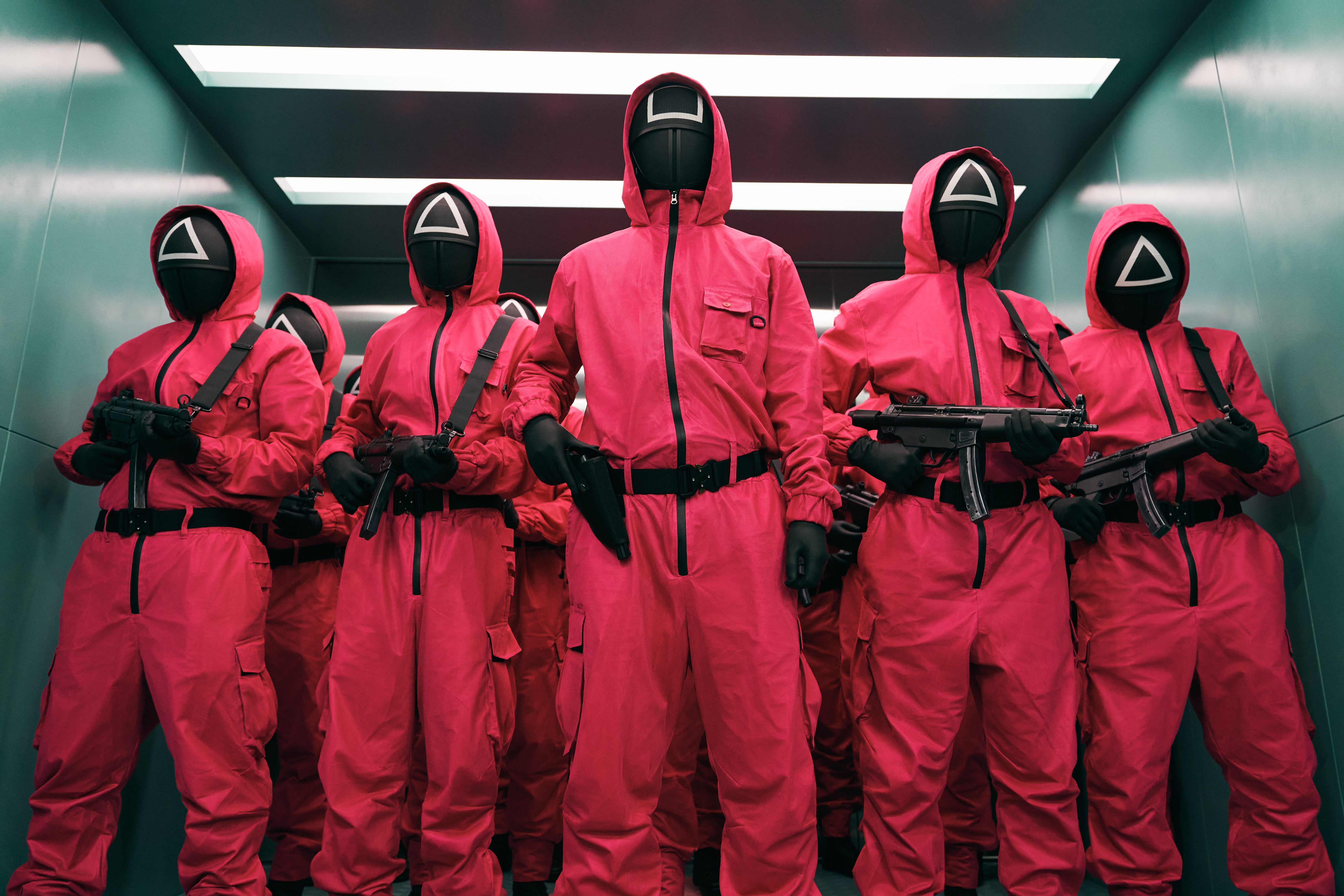 A group of people in red jumpsuits with hoods and masks featuring geometric shapes; still from 'Squid Game'
