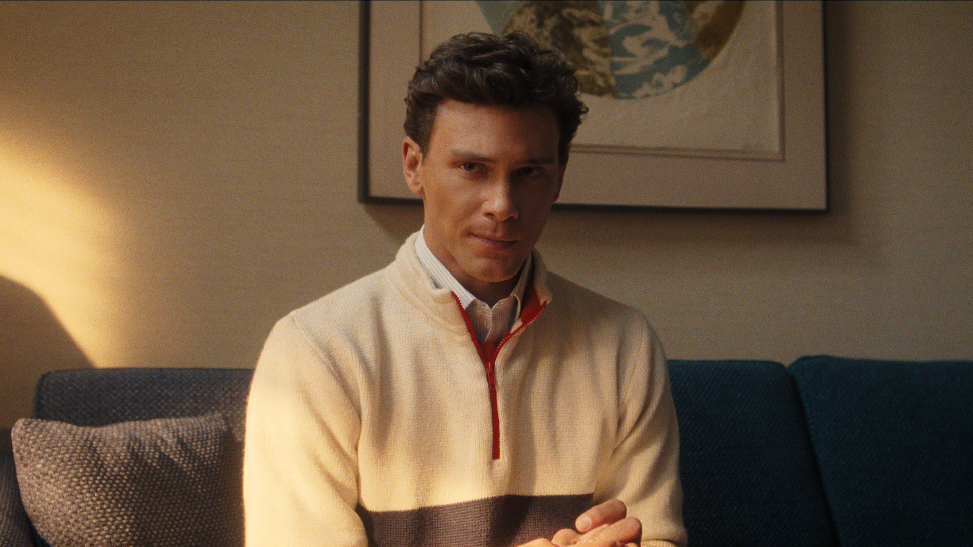A young man wearing a quarter zip and sitting on a couch, looking uncomfortable; Cooper Koch in 'Monsters: The Lyle and Erik Menendez Story'
