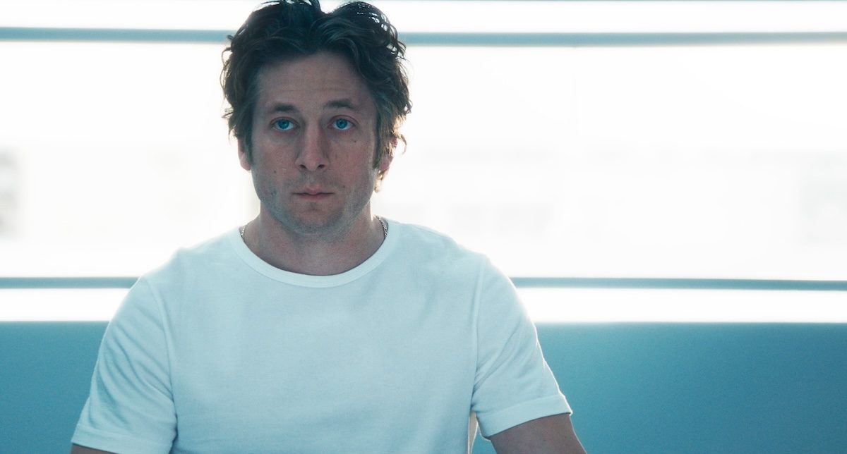 'The Bear' Season 4 stars Jeremy Allen White as Carmy Berzatto, shown here wearing a white t-shirt staring blankly ahead with a bright white backdrop behind him