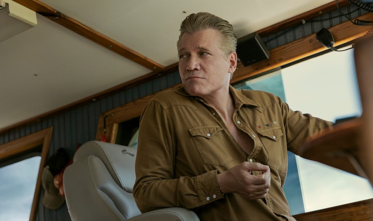 The Waterfront stars Holt McCallany as Harlan Buckley in the Netflix series. Here he's shown sitting in the captain's chair of a boat, wearing a brown button-down, looking over his right shoulder