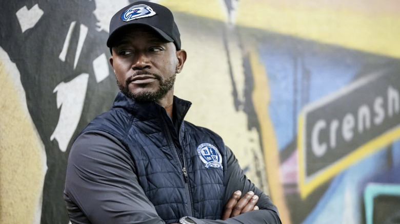 Coach Baker with his arms crossed leaning against a mural