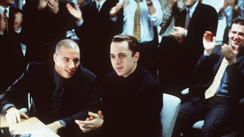 Chris talks to Seth surrounded by men clapping in Boiler Room (2000)