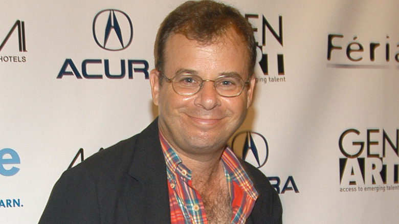 Rick Moranis smiles in suit coat and plaid shirt