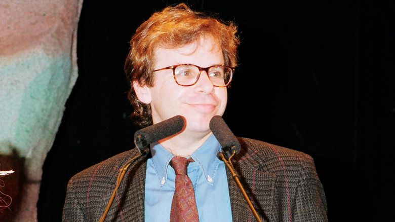 Rick Moranis stands in front of two microphones