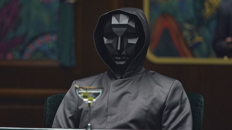 The Front Man in a mask with a drink in front of him on Squid Game