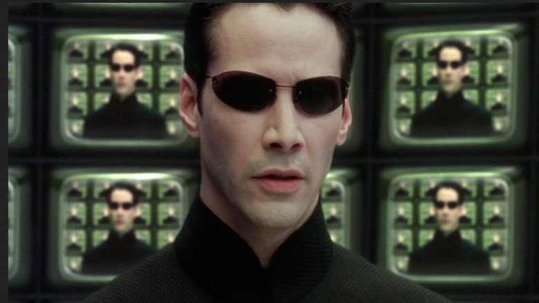 Neo surrounded by screens showing his own face in "The Matrix" (1999)