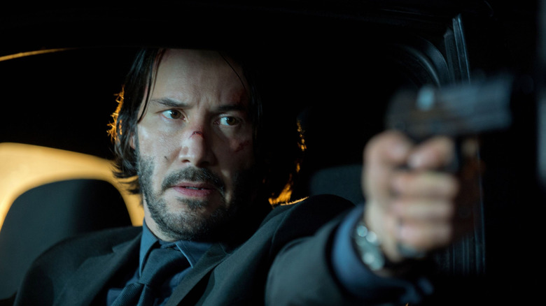 John Wick (Keanu Reeves) driving and pointing a gun out of his car window