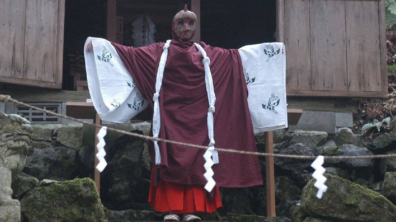 A figure is dressed in robes and a mask representing Kagutaba in "Noroi: The Curse" (2005)