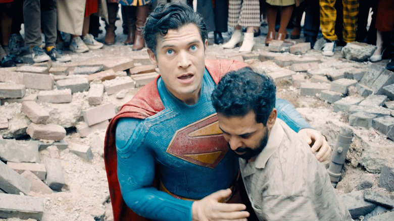Superman is helped up by a civilian amid rubble in Superman (2025)