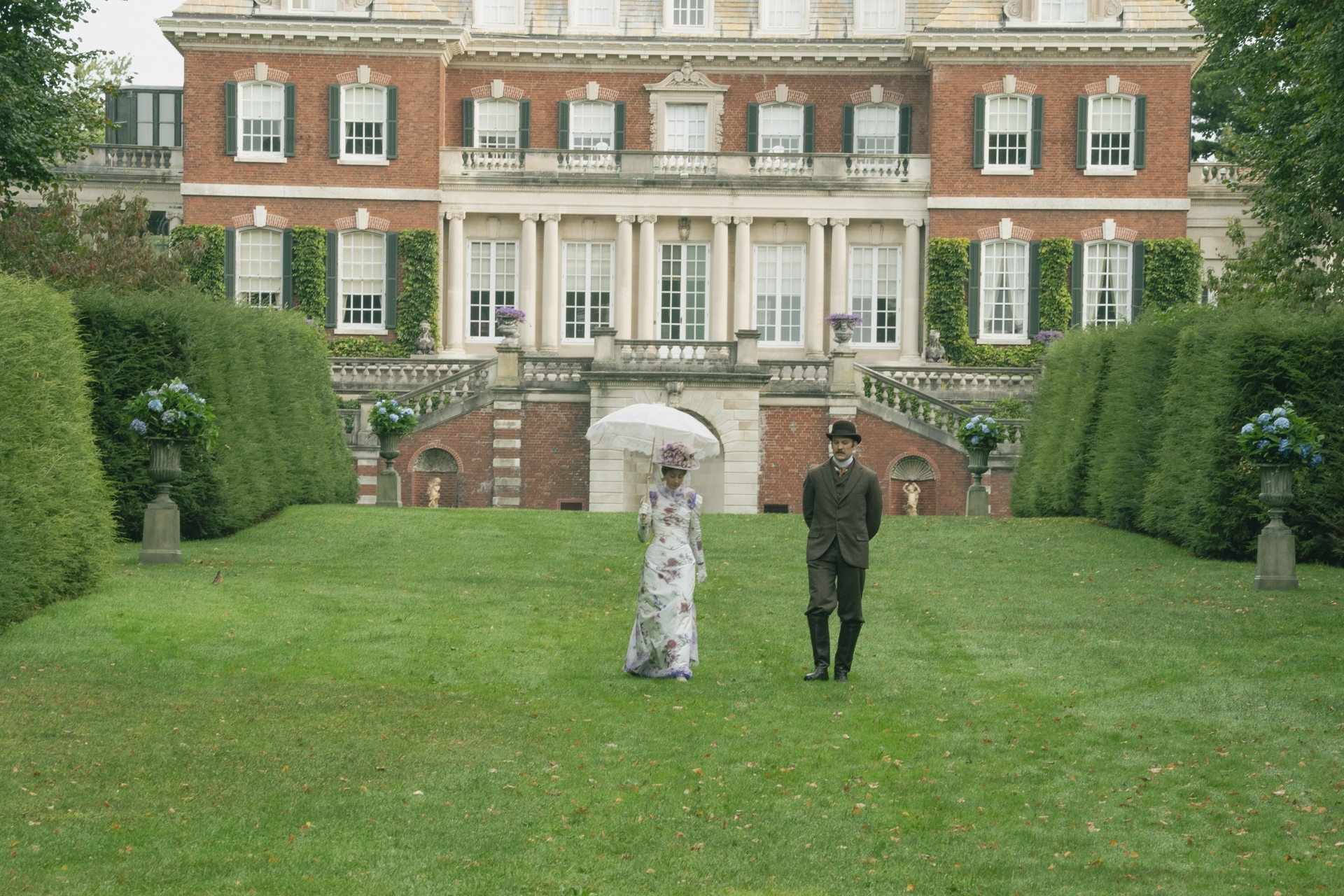 Carrie Coon and Ben Lamb walking in an English garden in 'The Gilded Age' on HBO. 
