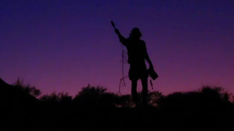 A figure holds up a microphone against a dark sky in "The Outwaters" (2022)