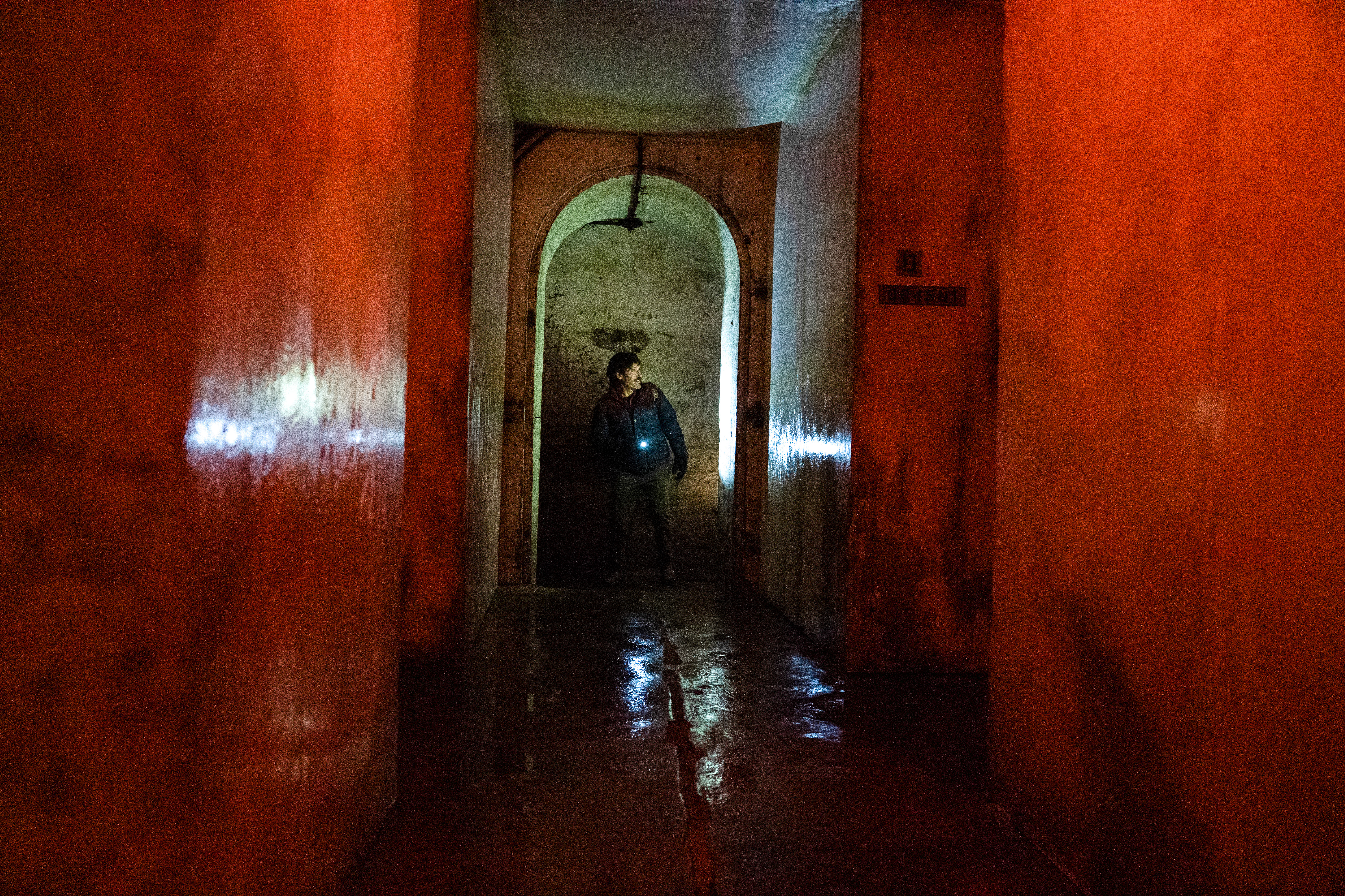 A concrete structure lit bright red with a man holding a flashlight standing in the center in the far end of the frame.