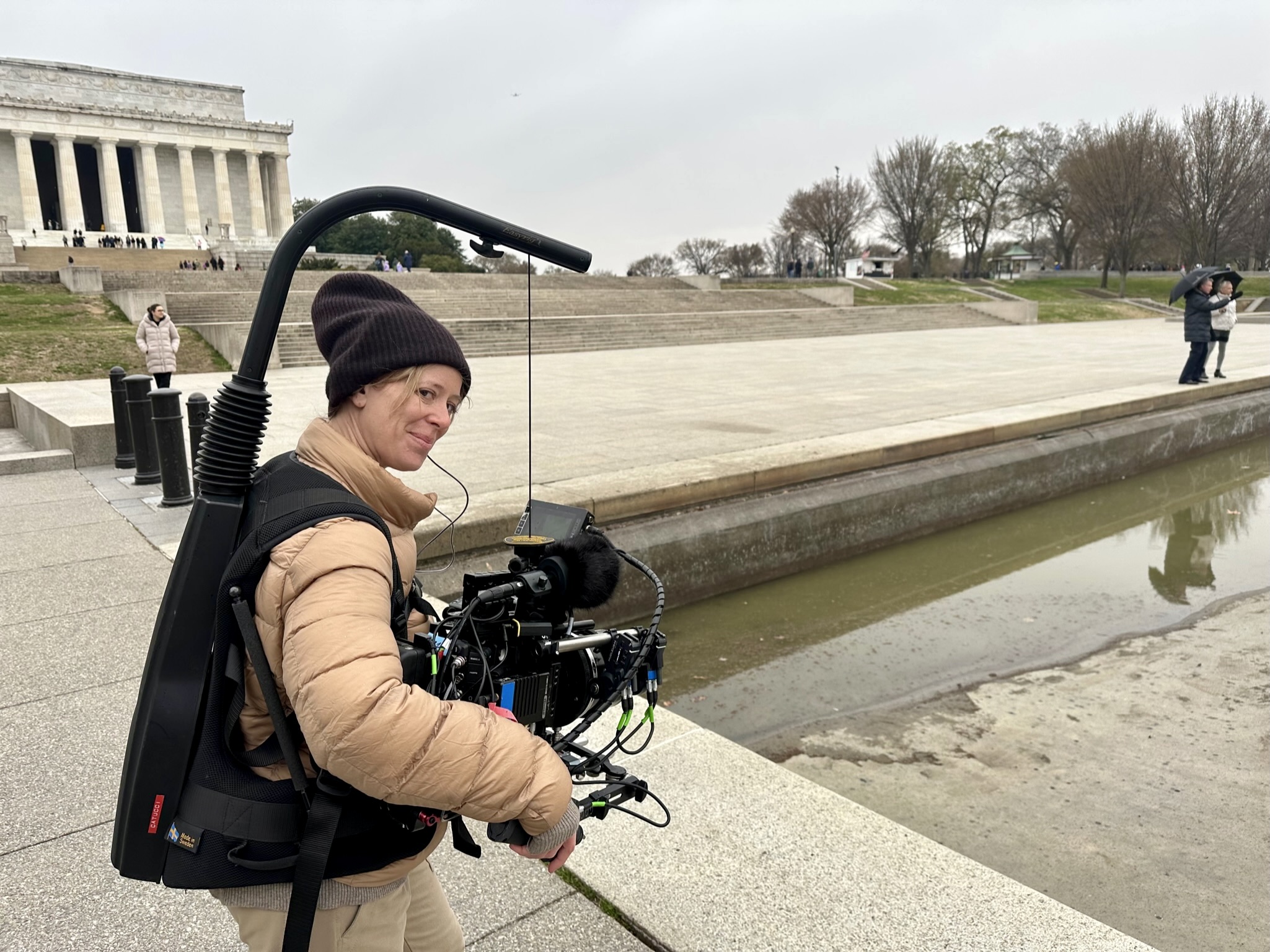 Cinematographer Zoe White holding a camera on a steadycam rig on the Washington Mall with the Lincoln Memorial in the background.