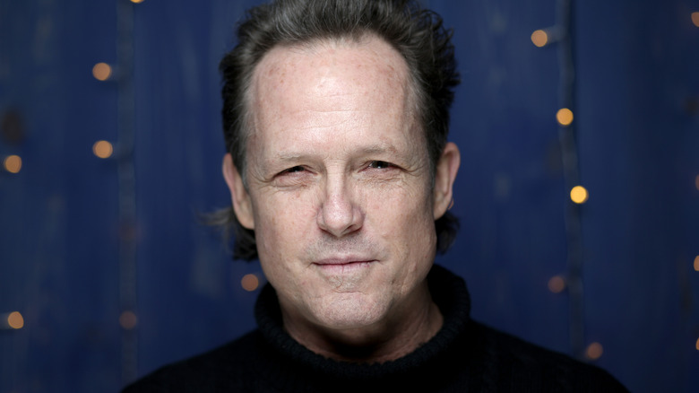 Dean Winters posing in front of a blue background