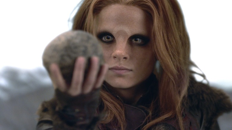 Irisa Nyira holding up a stone and looking at it in "Defiance"