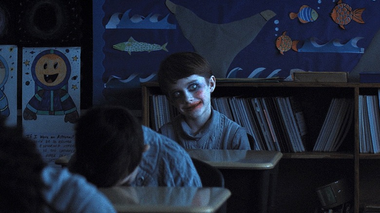 Alex smiling creepily with clown makeup on in the classroom in Weapons