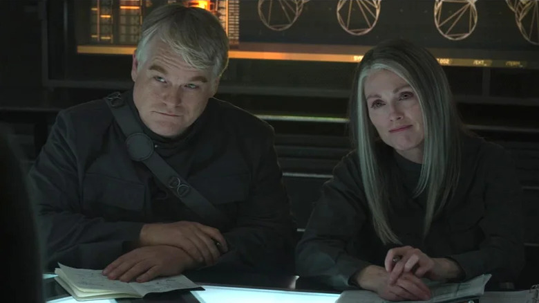 Plutarch Heavensbee sits beside Alma Coin in "The Hunger Games: Mockingjay - Part 1" (2014)