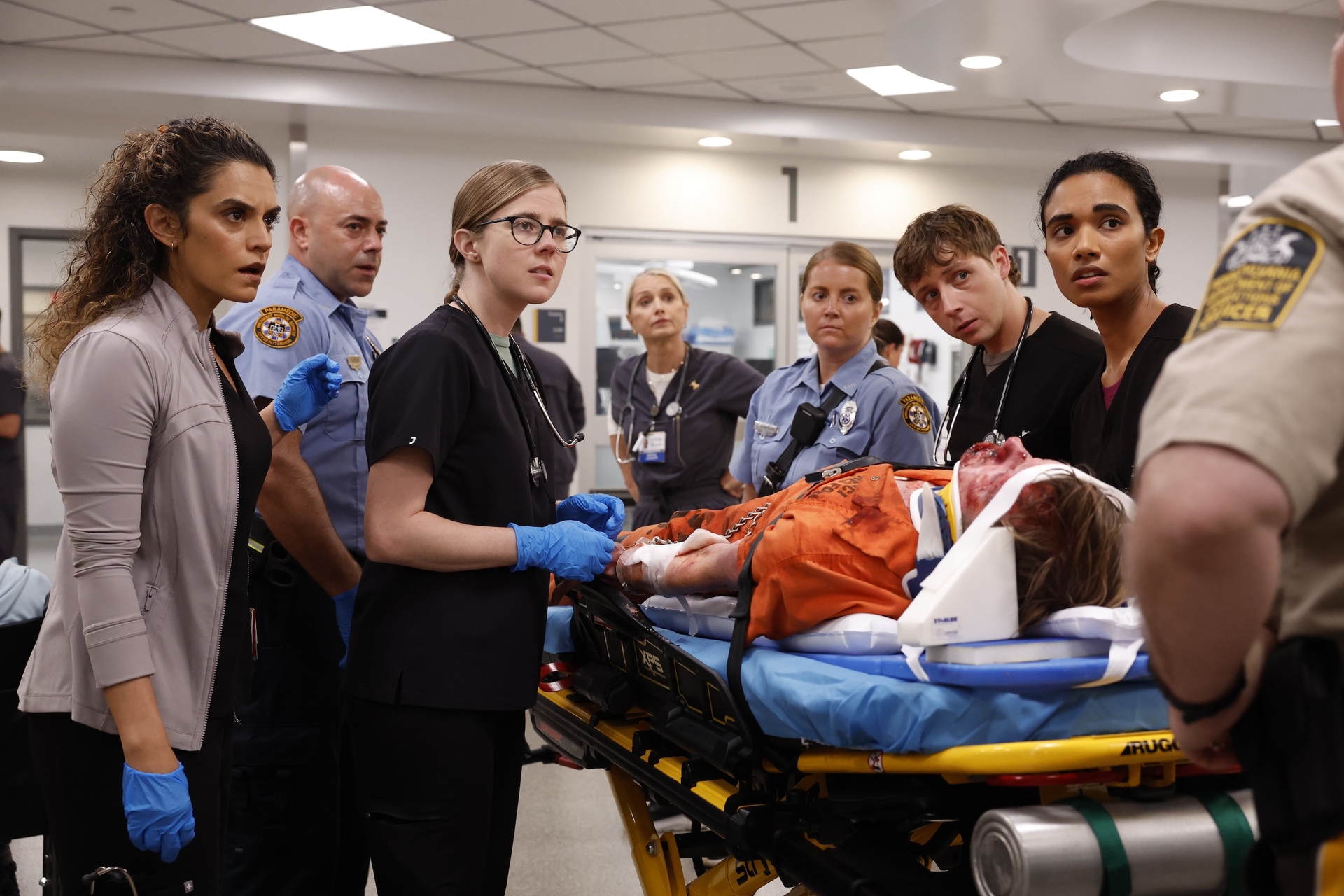 A group of doctors, nurses, and police officers around a body on a gurney; still from 'The Pitt'