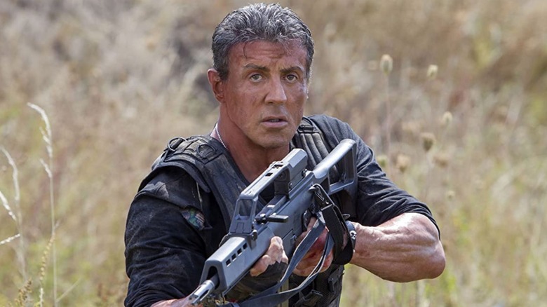 Ross holds a machine gun in a wheat field in "The Expendables" (2010)