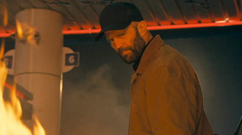 Clay looks down and sneers with flames around him in "The Beekeeper" (2024)