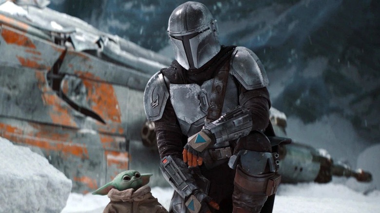 Din Djarin kneels by Grogu and a ship in "The Mandalorian" (2019-present)