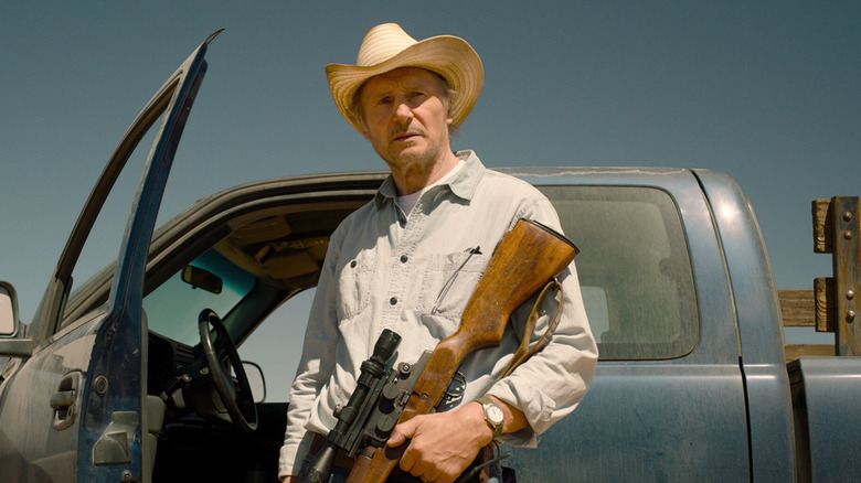 Hanson holds a rifle outside his pickup truck in "The Marksman" (2021)
