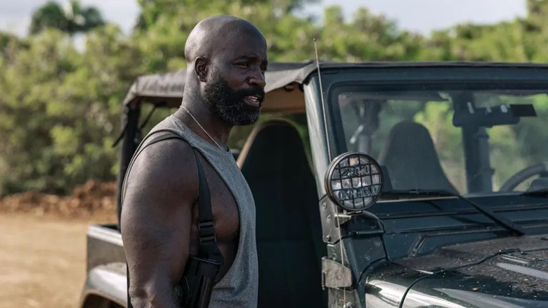 Gaspare stands by a jeep near a treeline in "Plane" (2023)