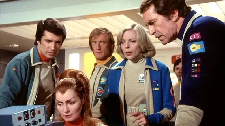 The crew of Moonbase Alpha gather around a computer console in Space:1999