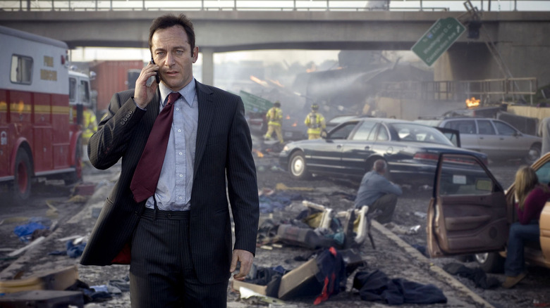 Brydon talks on his cel phone while walking through debris on the street in The State Within